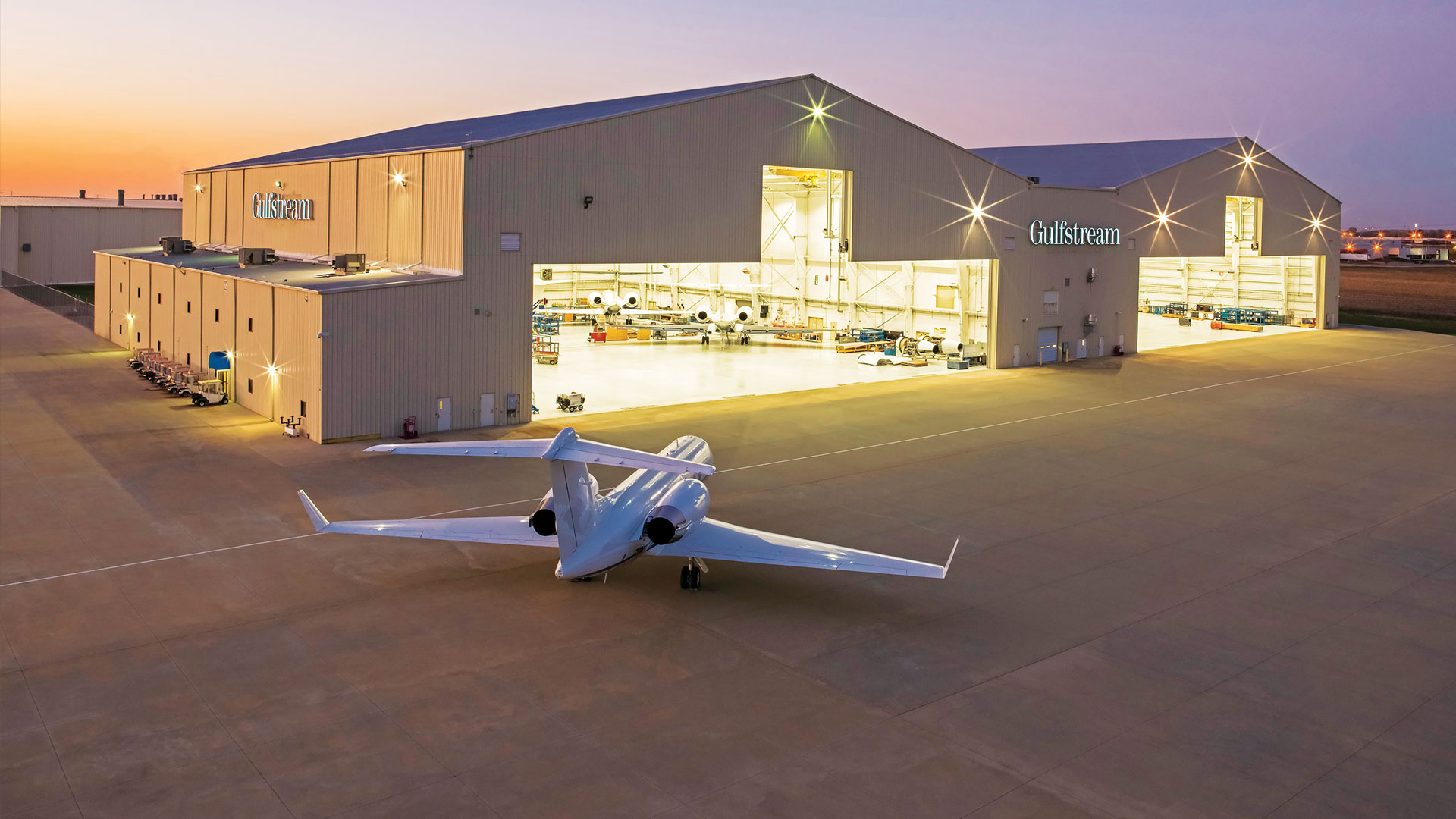 A Gulfstream jet sits outside a hanger in either dusk or dawn.