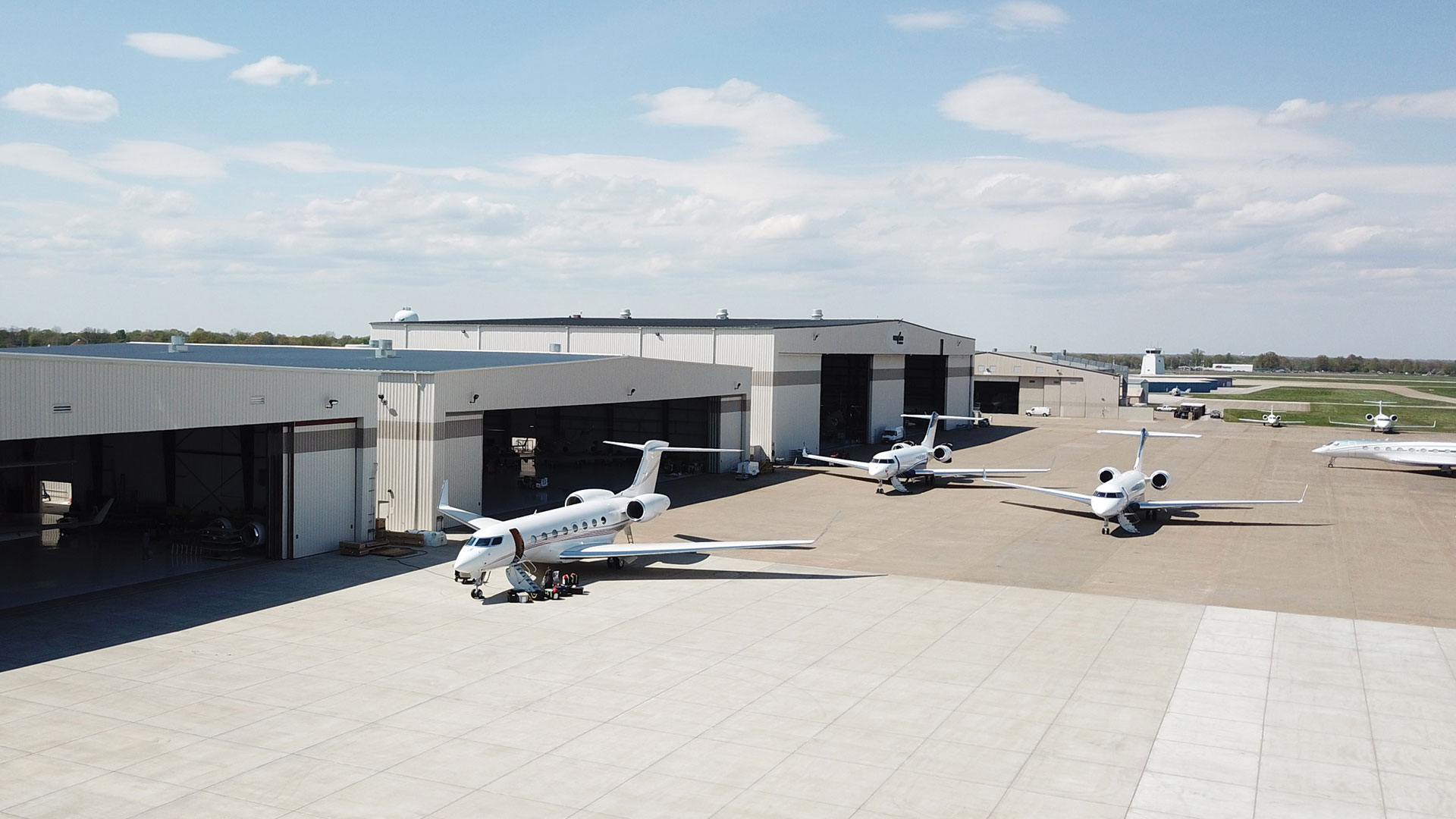 Exterior of a West Star hanger in the daytime with a few jets parked.