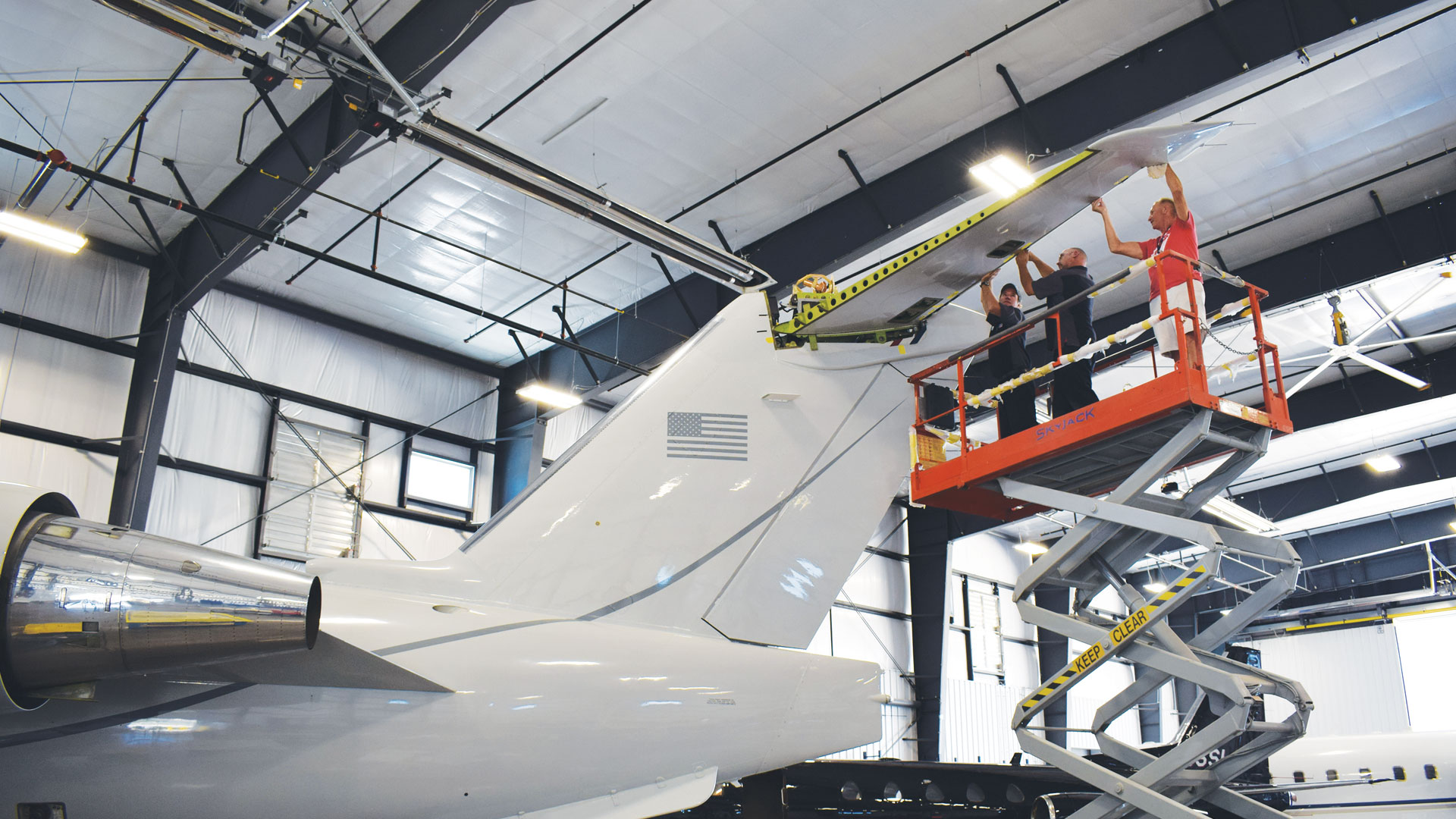 Workers on a lift installing a rear wing on aircraft.