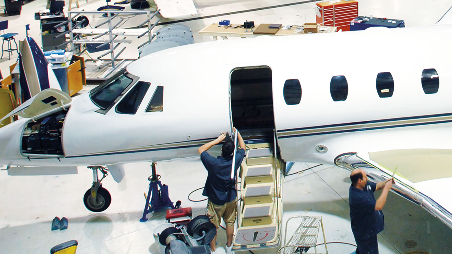 Workers working on the door and wing of a jet.