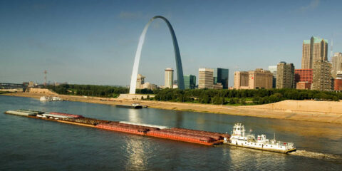 Tug boat pushing barge down Mississippi River in front of Gateway Arch and skyline of St. Louis