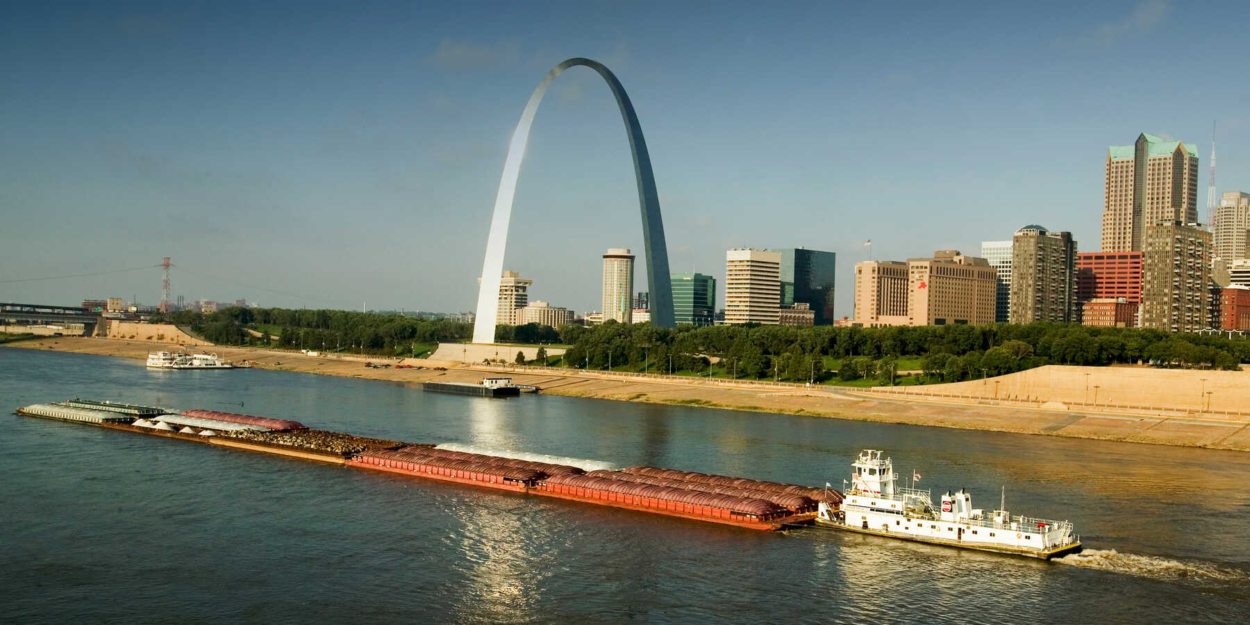 Tug boat pushing barge down Mississippi River in front of Gateway Arch and skyline of St. Louis